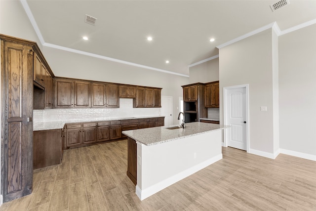 kitchen featuring light wood-type flooring, sink, an island with sink, and light stone counters