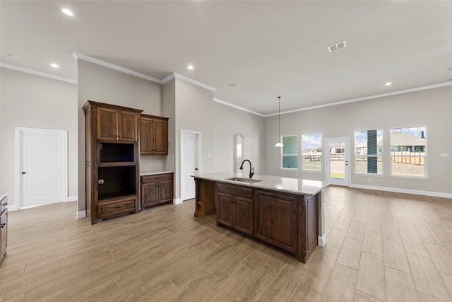 kitchen featuring a center island with sink, sink, light stone countertops, crown molding, and light wood-type flooring