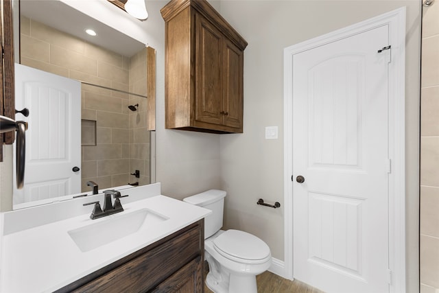 bathroom with toilet, hardwood / wood-style floors, vanity, and a tile shower