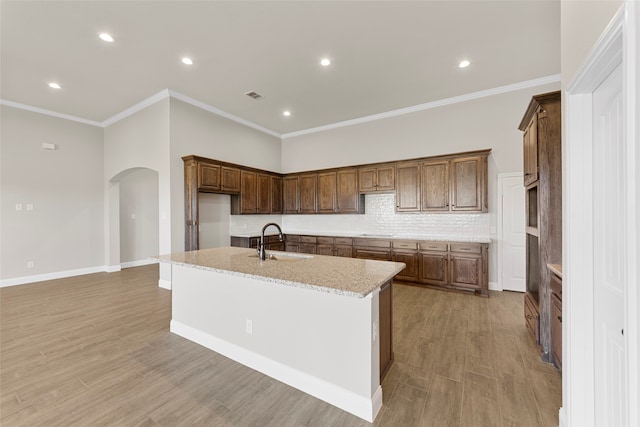 kitchen with light hardwood / wood-style flooring, light stone countertops, sink, and an island with sink