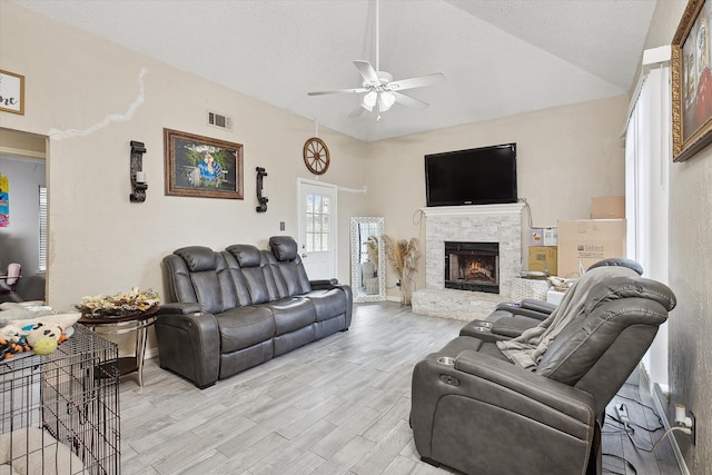 living room featuring lofted ceiling, ceiling fan, a textured ceiling, light hardwood / wood-style flooring, and a stone fireplace