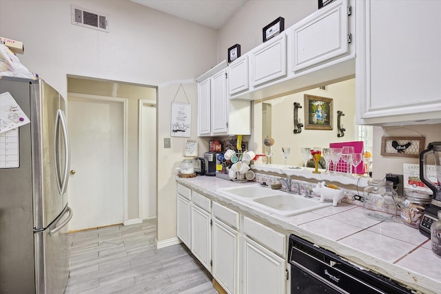 kitchen featuring white cabinets, tile countertops, black dishwasher, and stainless steel fridge