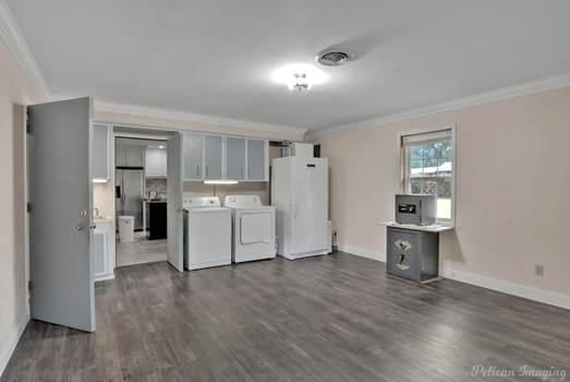 clothes washing area with washing machine and dryer, visible vents, ornamental molding, and dark wood finished floors