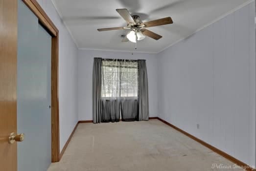 empty room with ornamental molding, light colored carpet, a ceiling fan, and baseboards