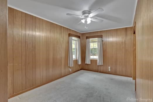 carpeted spare room with ceiling fan and wood walls