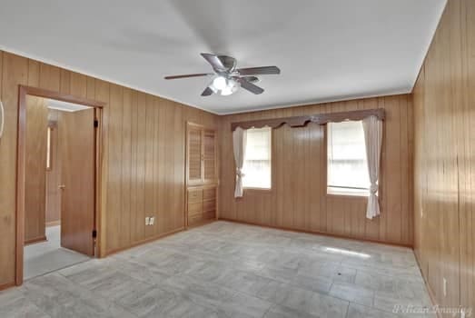 unfurnished room featuring a ceiling fan and wood walls