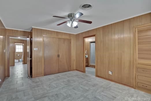 unfurnished bedroom with wood walls, ceiling fan, visible vents, and a closet