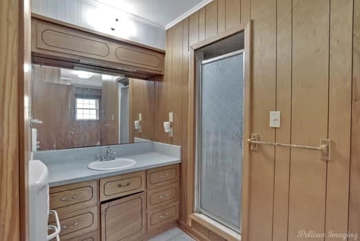 bathroom with wooden walls, crown molding, vanity, and a shower stall