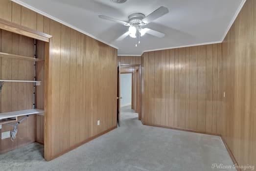 interior space featuring crown molding, ceiling fan, light colored carpet, and wood walls