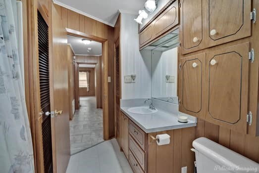 bathroom with toilet, wood walls, ornamental molding, vanity, and tile patterned flooring