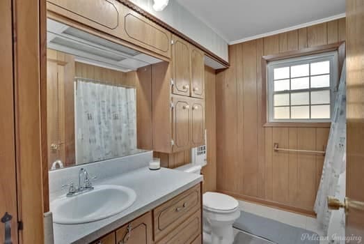 full bath with wooden walls, curtained shower, vanity, and toilet