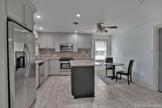 kitchen featuring a kitchen island, stainless steel appliances, backsplash, gray cabinets, and ceiling fan