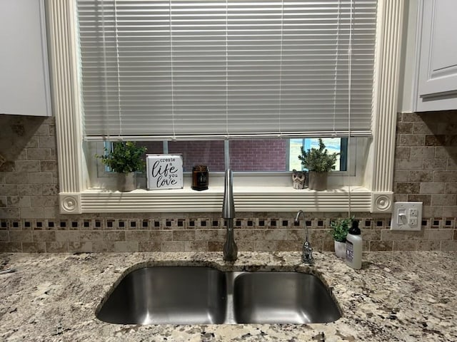 interior details with a sink, white cabinetry, light stone counters, and backsplash