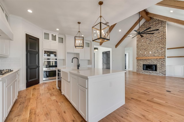 kitchen with a fireplace, white cabinetry, tasteful backsplash, a center island with sink, and pendant lighting