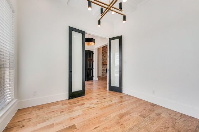 unfurnished room with french doors, an inviting chandelier, and light wood-type flooring