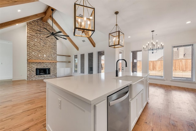 kitchen featuring an island with sink, stainless steel dishwasher, a brick fireplace, hanging light fixtures, and beam ceiling