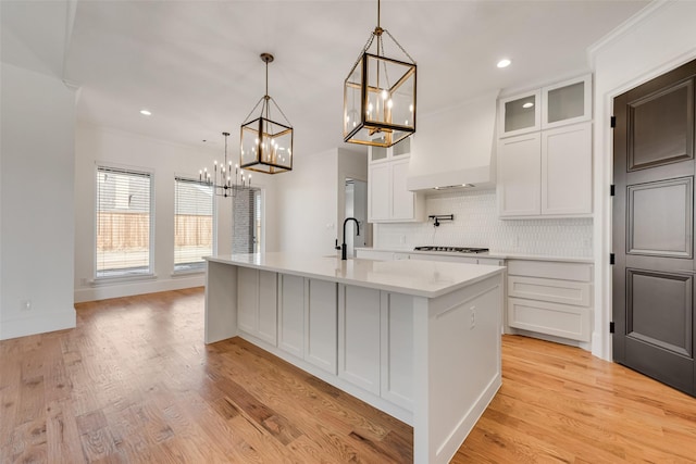 kitchen with sink, white cabinetry, light hardwood / wood-style flooring, hanging light fixtures, and a center island with sink