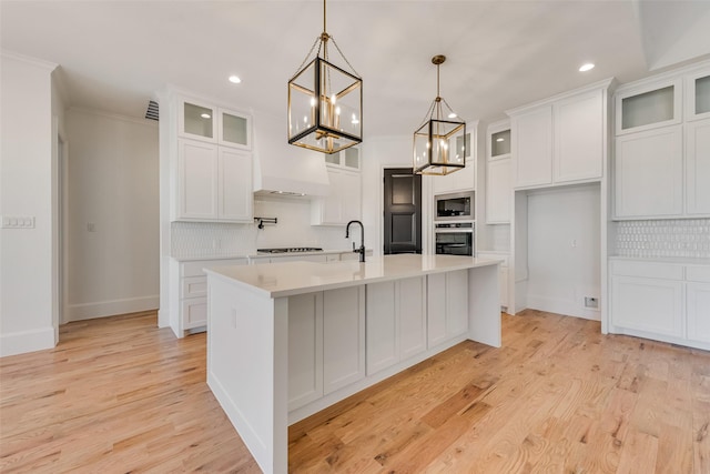 kitchen with stainless steel oven, white cabinetry, an island with sink, pendant lighting, and built in microwave