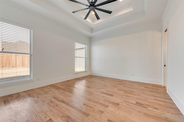 empty room with ornamental molding, a raised ceiling, ceiling fan, and light hardwood / wood-style floors