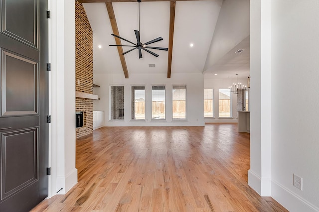 unfurnished living room with light wood-type flooring, ceiling fan with notable chandelier, a brick fireplace, high vaulted ceiling, and beam ceiling