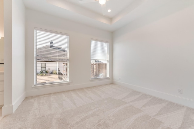 carpeted empty room with ceiling fan, plenty of natural light, and a tray ceiling