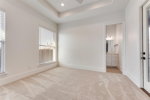 unfurnished bedroom featuring ceiling fan, connected bathroom, light carpet, and a tray ceiling