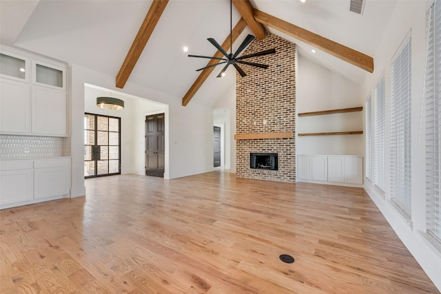 unfurnished living room with a brick fireplace, high vaulted ceiling, beam ceiling, light wood-type flooring, and ceiling fan