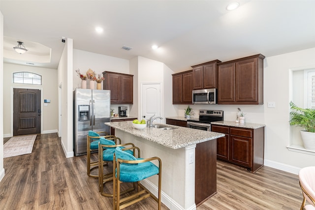 kitchen featuring an island with sink, wood-type flooring, light stone countertops, a kitchen bar, and appliances with stainless steel finishes