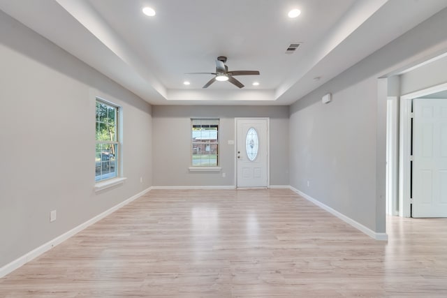 entryway with plenty of natural light, ceiling fan, a tray ceiling, and light wood-type flooring