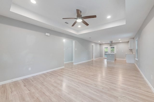 unfurnished living room featuring ceiling fan, light hardwood / wood-style floors, and a raised ceiling