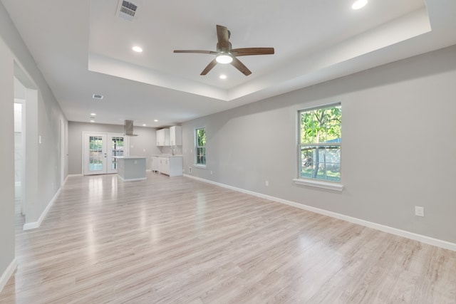 unfurnished living room featuring light hardwood / wood-style flooring, a raised ceiling, and a wealth of natural light