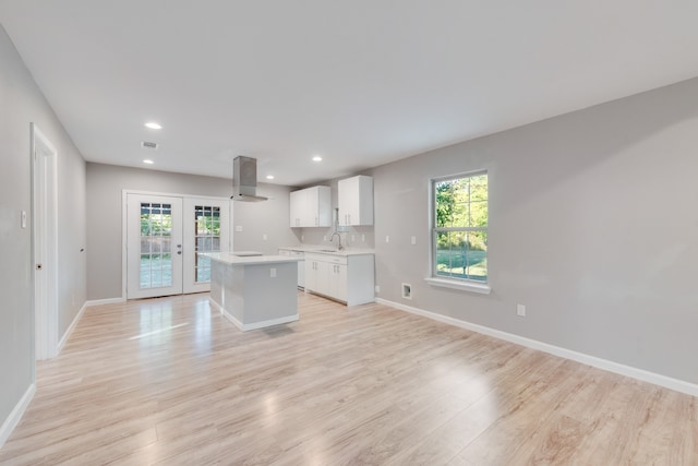 kitchen with a kitchen island, french doors, wall chimney exhaust hood, light hardwood / wood-style flooring, and white cabinetry