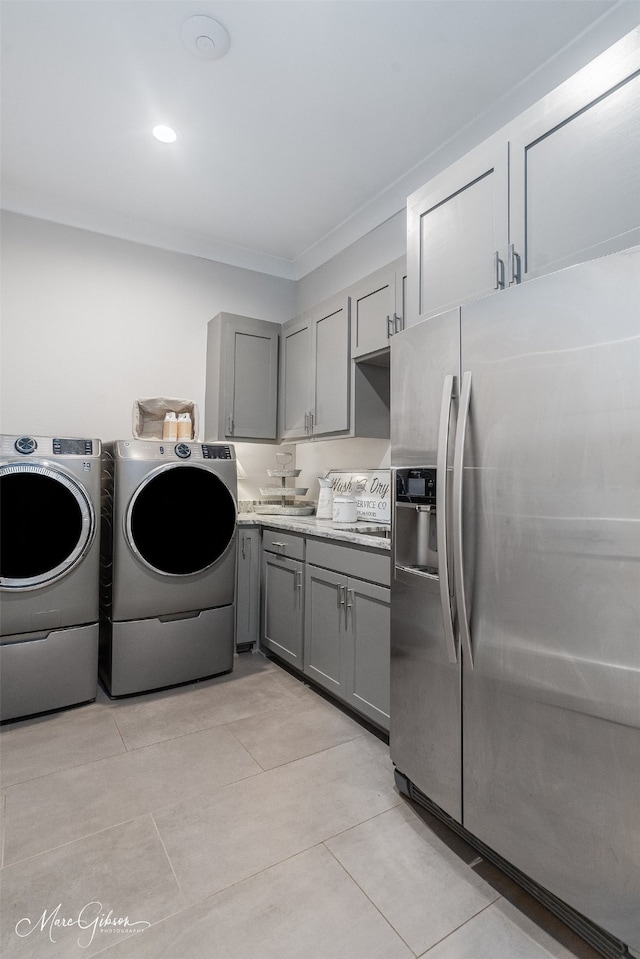 washroom with light tile patterned floors, ornamental molding, washing machine and dryer, and cabinets