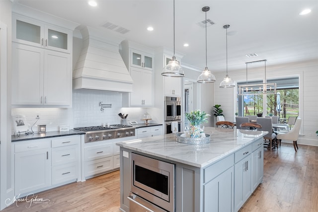 kitchen with pendant lighting, premium range hood, white cabinetry, stainless steel appliances, and a kitchen island