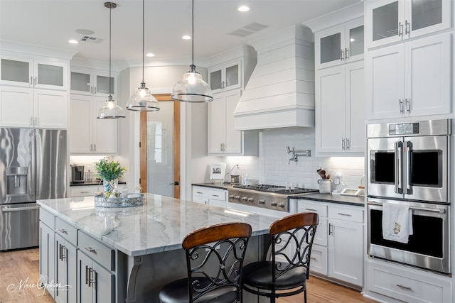 kitchen featuring appliances with stainless steel finishes, a center island, custom range hood, white cabinets, and dark stone counters