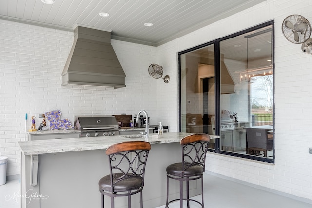 kitchen featuring sink, light stone counters, ornamental molding, a kitchen breakfast bar, and custom range hood