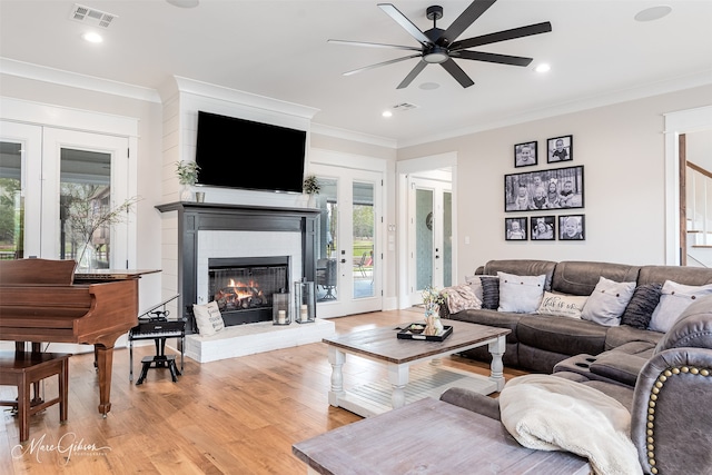 living room featuring crown molding, a fireplace, light hardwood / wood-style floors, and ceiling fan