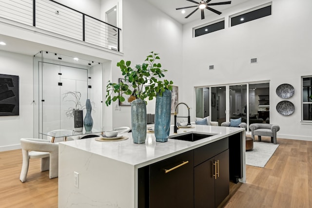 kitchen featuring sink, a kitchen island, ceiling fan, a high ceiling, and light hardwood / wood-style flooring