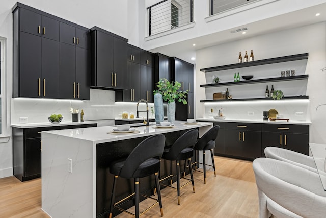 kitchen with a breakfast bar, tasteful backsplash, light wood-type flooring, and an island with sink