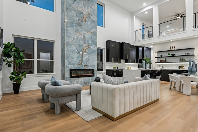 living room featuring a tiled fireplace, a towering ceiling, and light hardwood / wood-style flooring