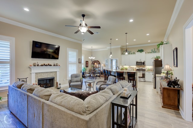 living room with crown molding, ceiling fan with notable chandelier, light hardwood / wood-style floors, and a wealth of natural light