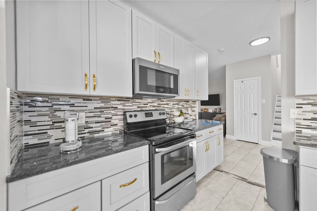 kitchen with stainless steel appliances, backsplash, dark stone counters, light tile patterned floors, and white cabinetry