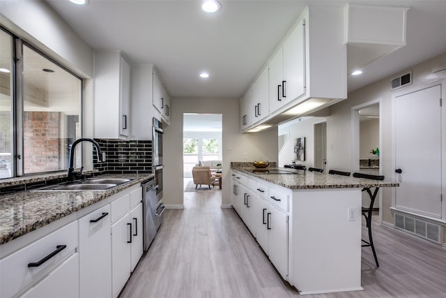 kitchen featuring a breakfast bar area, white cabinetry, sink, and light hardwood / wood-style floors