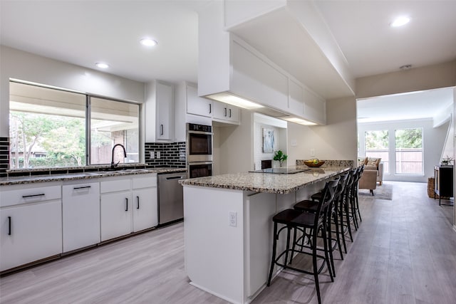 kitchen featuring white cabinets, light stone countertops, light hardwood / wood-style floors, a kitchen bar, and stainless steel appliances