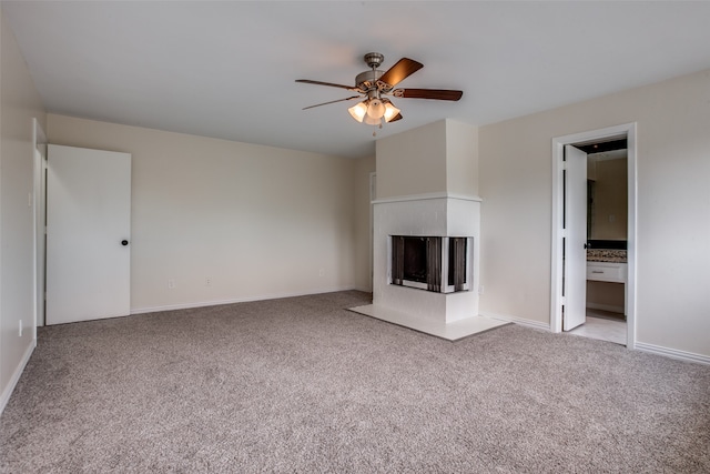 unfurnished living room with a multi sided fireplace, ceiling fan, and light colored carpet