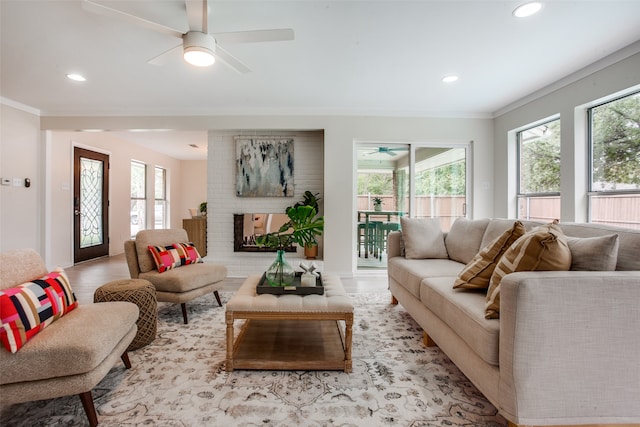 living room with light hardwood / wood-style floors, a brick fireplace, ceiling fan, and ornamental molding