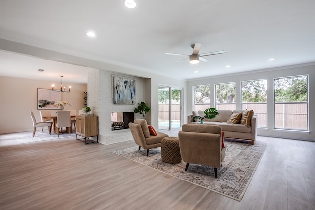 living room featuring a healthy amount of sunlight, a fireplace, light hardwood / wood-style floors, and ceiling fan with notable chandelier