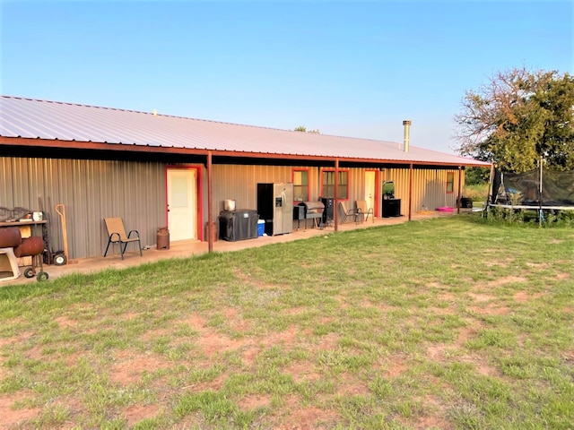 back of property with a trampoline and a yard