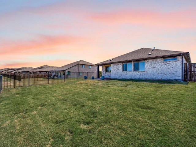 rear view of house with a fenced backyard, a yard, and brick siding