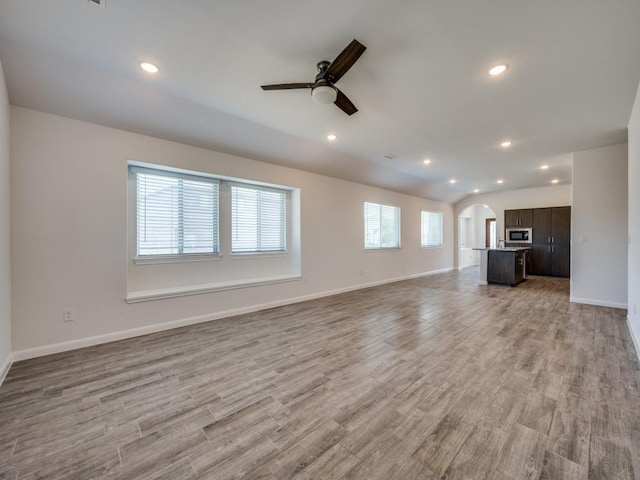 unfurnished living room featuring baseboards, recessed lighting, arched walkways, and light wood-type flooring